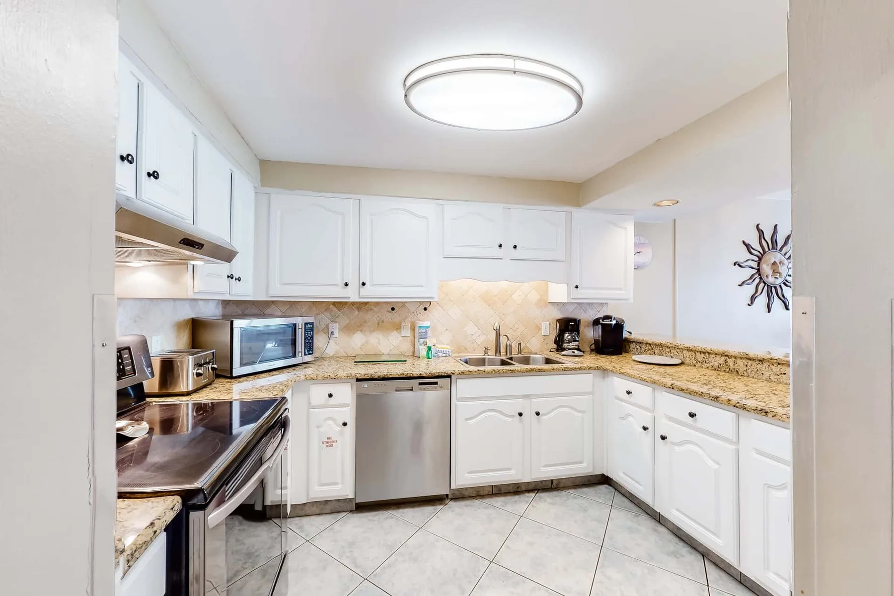 A bright kitchen with white cabinets, tiled flooring, and stainless steel appliances.