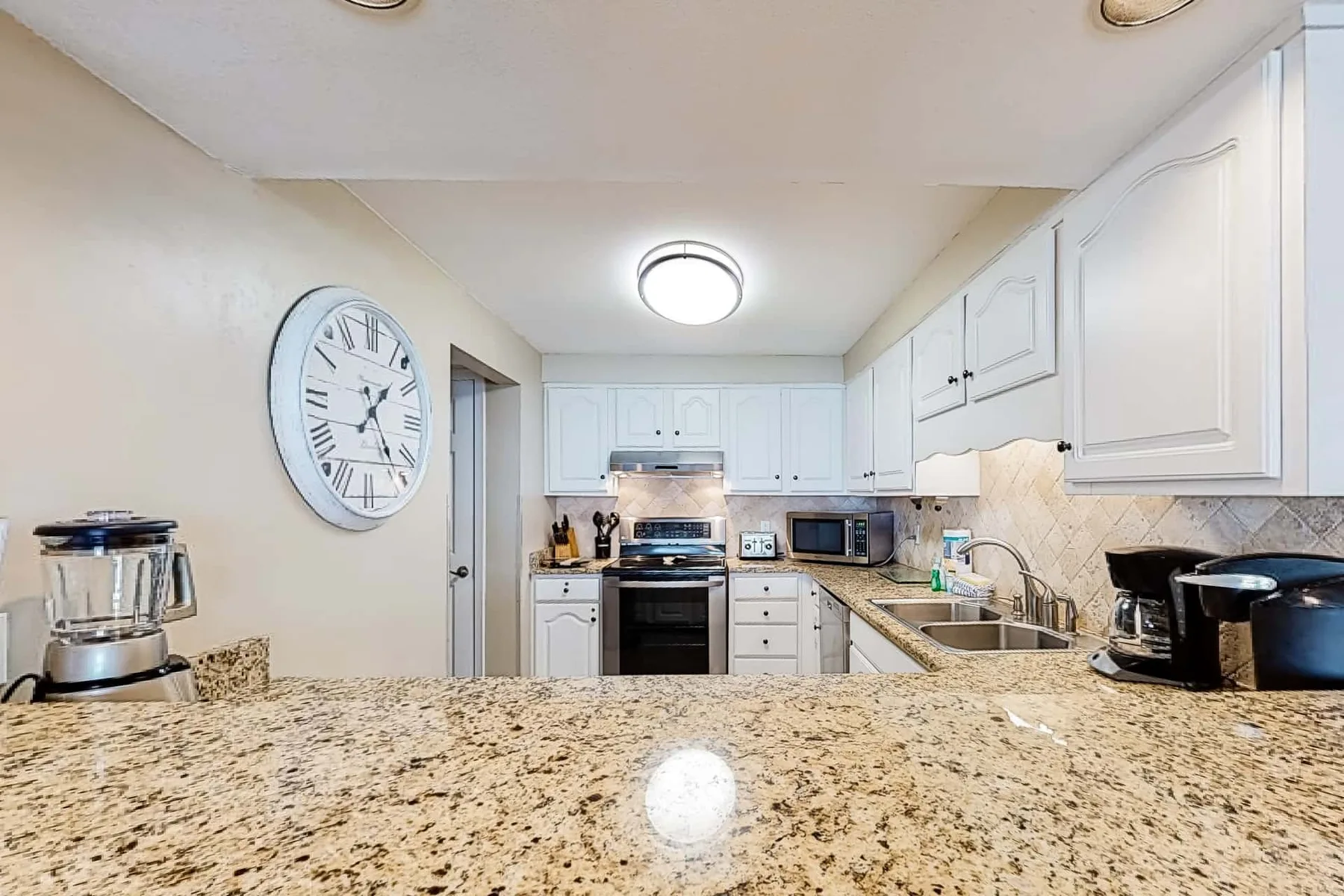 A bright kitchen with white cabinetry, stainless appliances, and a wide stone countertop.