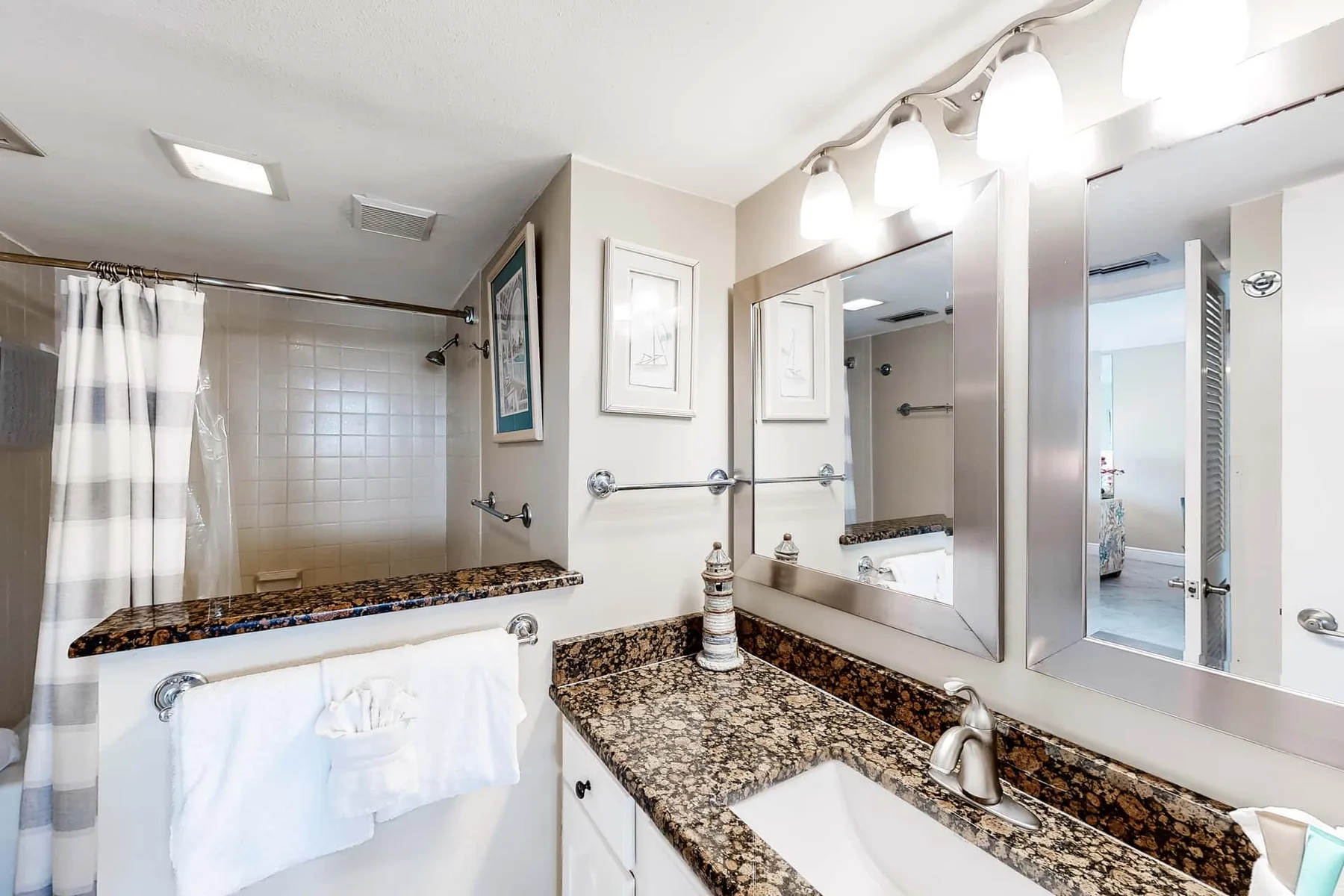 A bathroom vanity with a wide mirror and a curtained shower.