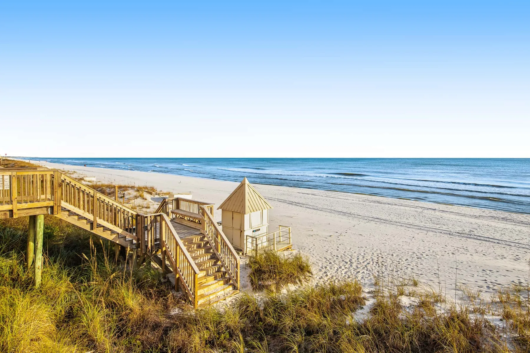 A beach access walkway crosses the dunes beside a broad sandy shoreline.