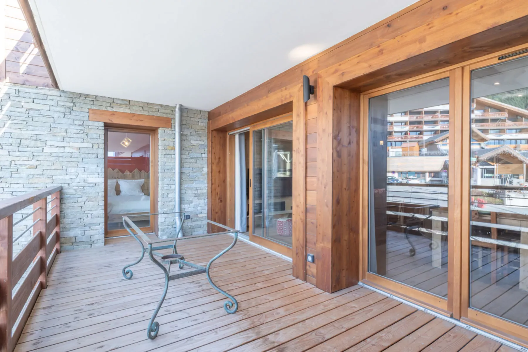 A wooden deck with a glass table sits beside large sliding glass doors.