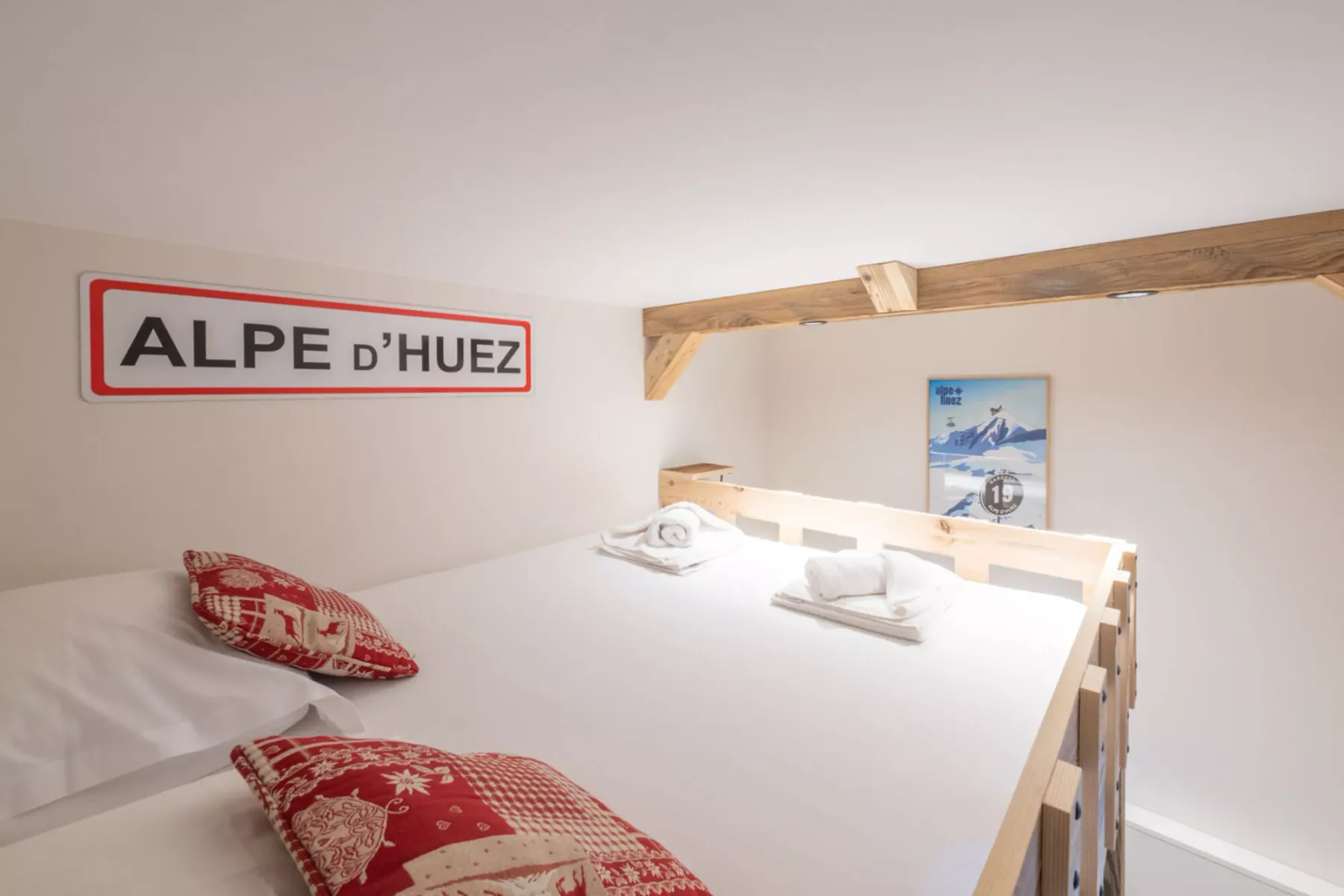 A bedroom with white bedding, red patterned pillows, and a wooden bed frame.