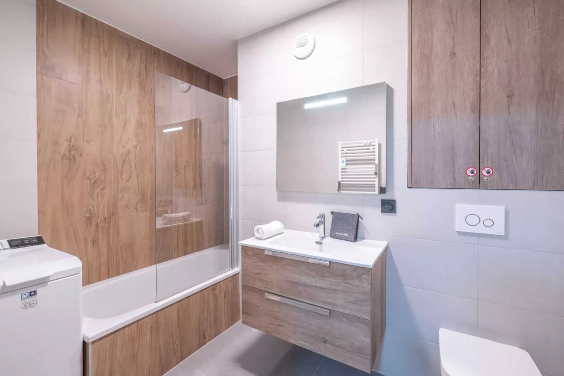 A modern bathroom with a bathtub, vanity, and washing machine.