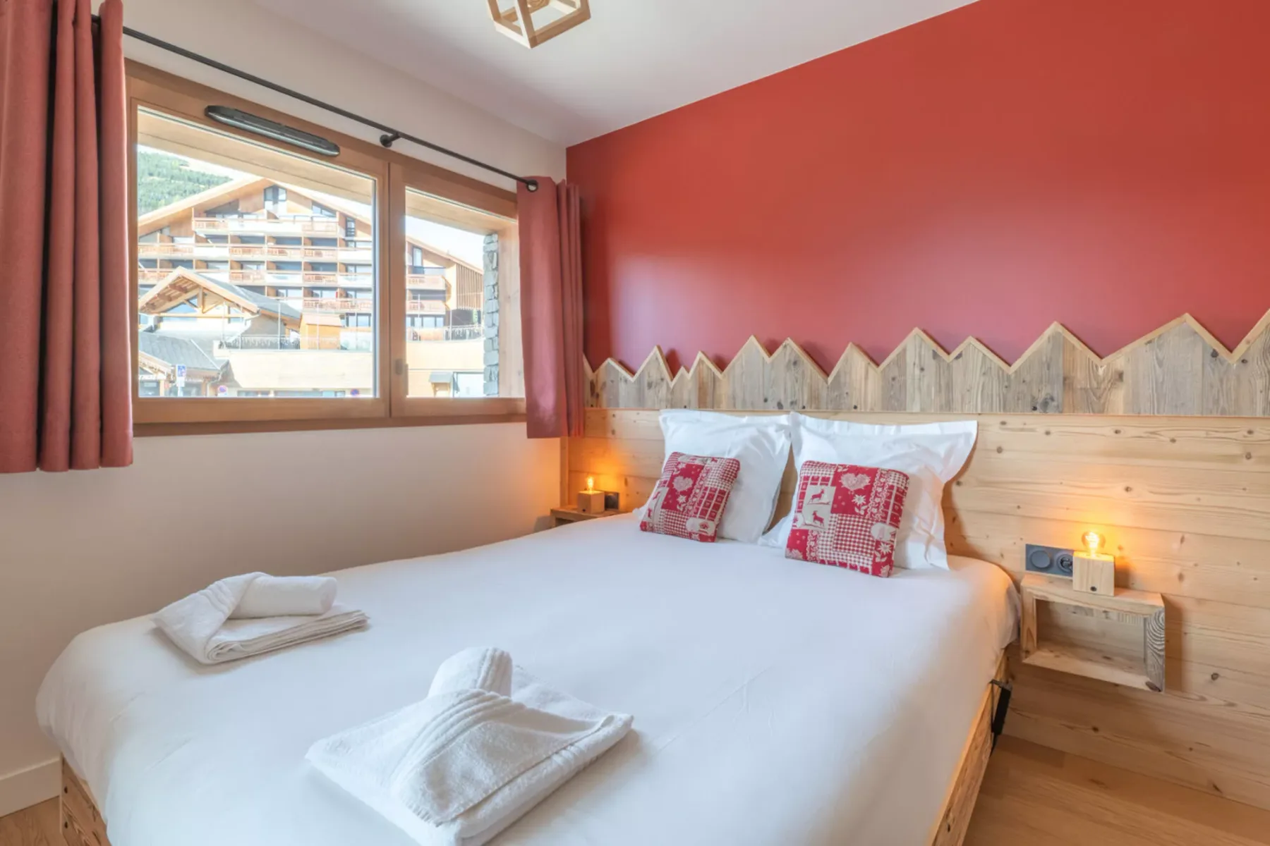 A bedroom with a bed beneath a red accent wall and a window.