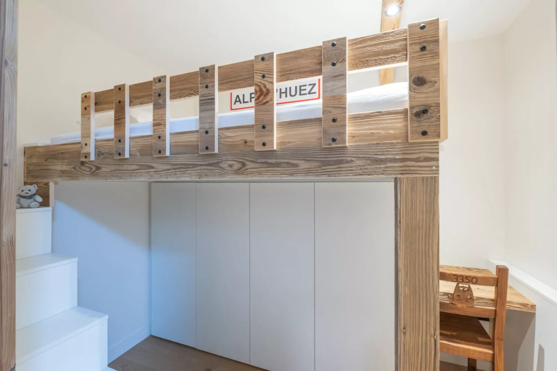 A lofted bed area with a wooden guardrail above built-in cabinetry and a desk.