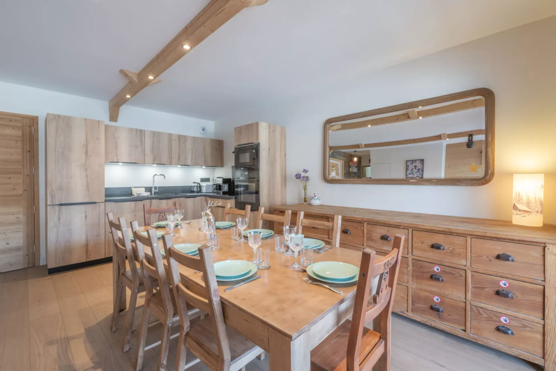 A dining area with a wooden table set with plates and glassware.