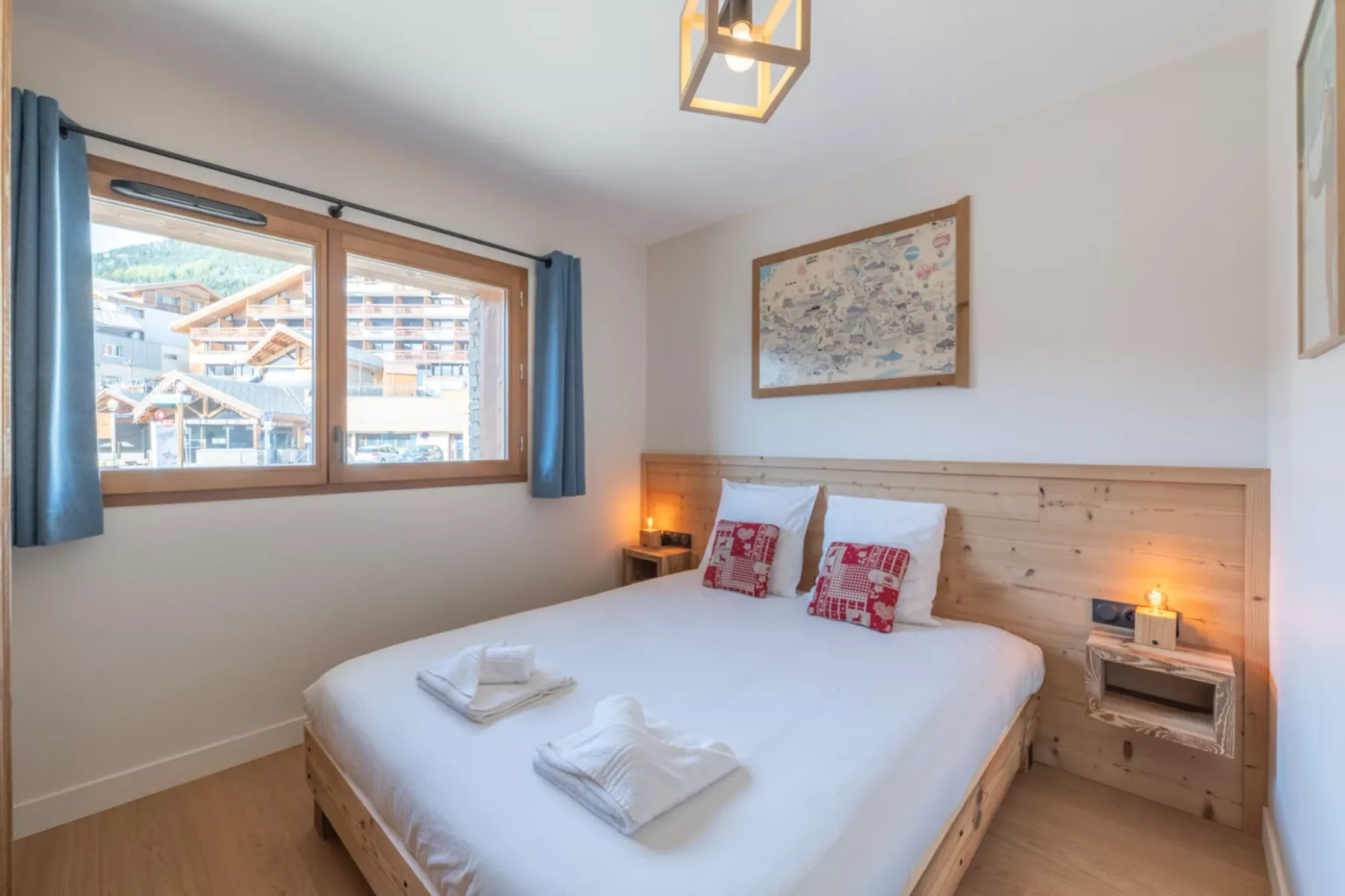 A bedroom with a bed, bedside lighting, and a window overlooking nearby buildings.