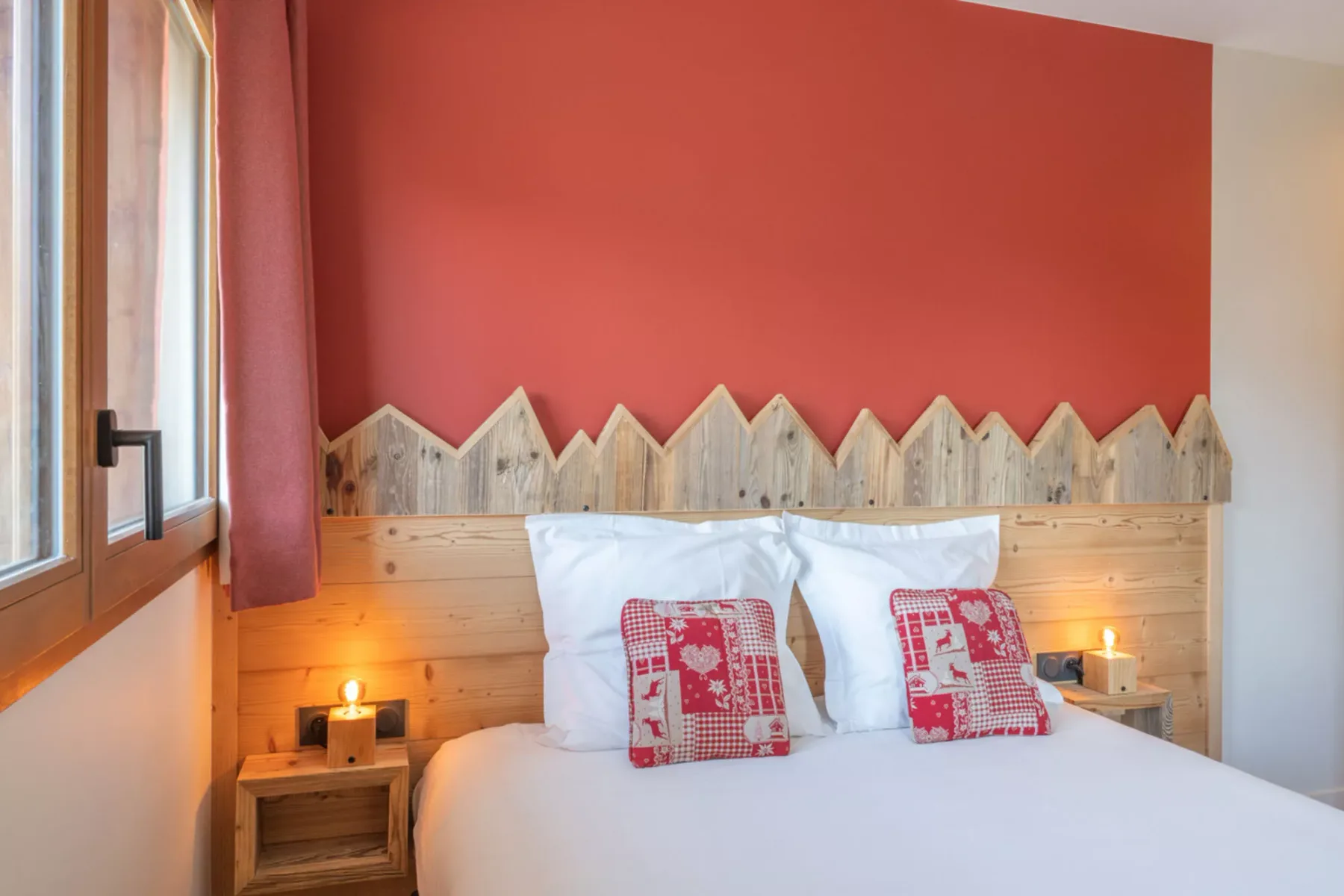 A bedroom with a bed beneath a red accent wall and a window.