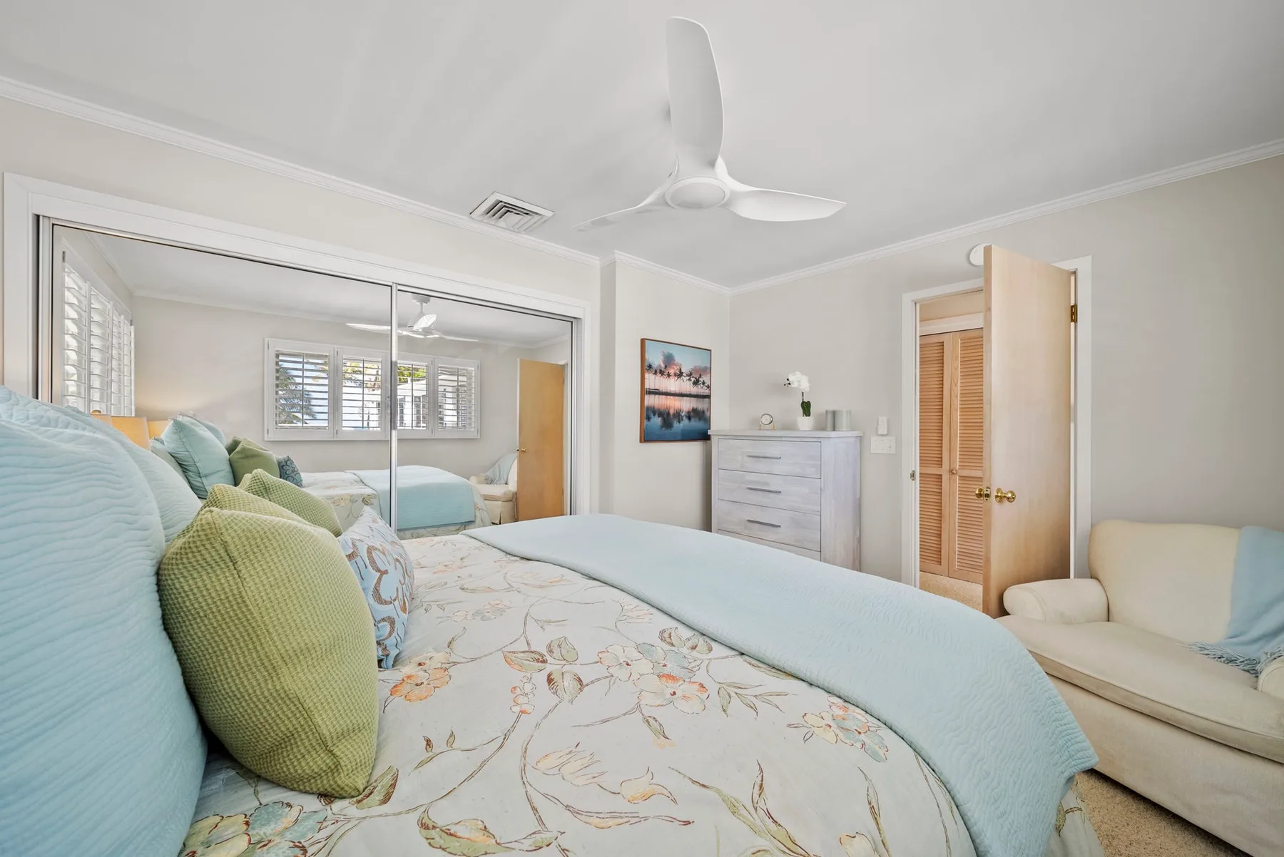 Un dormitorio luminoso con una cama, ropa de cama clara y un ventilador de techo.