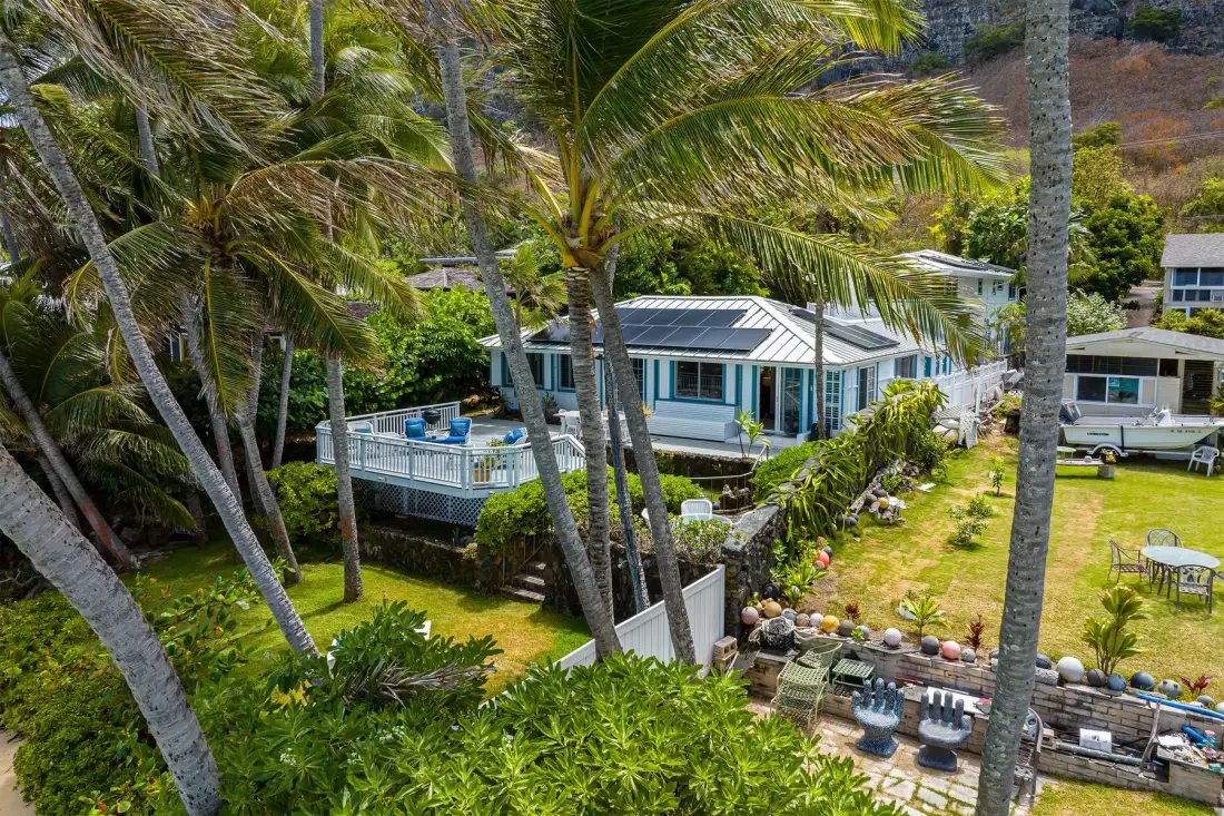 Vista aérea de una casa con techo blanco rodeada de palmeras y jardines.