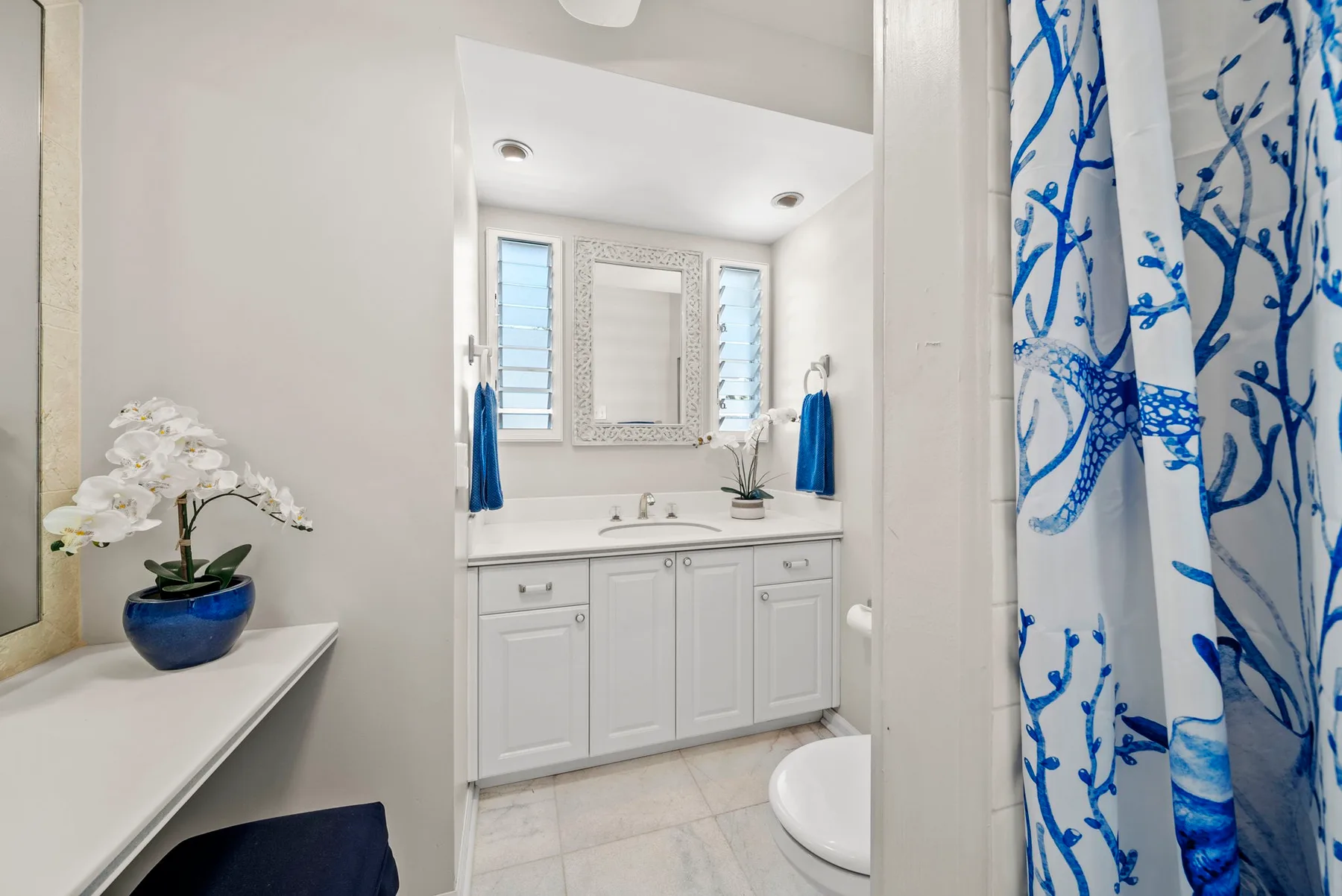 Un baño luminoso con tocador, espejo y cortina de ducha con estampado azul.