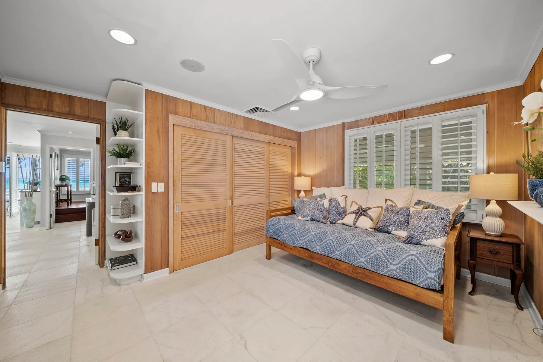 Un dormitorio con una cama de madera, ropa de cama estampada y ventanas con contraventanas.