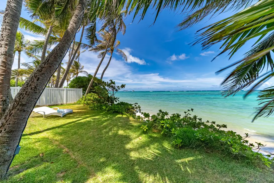 Una playa tropical bordeada de palmeras, con césped junto a aguas turquesas claras.