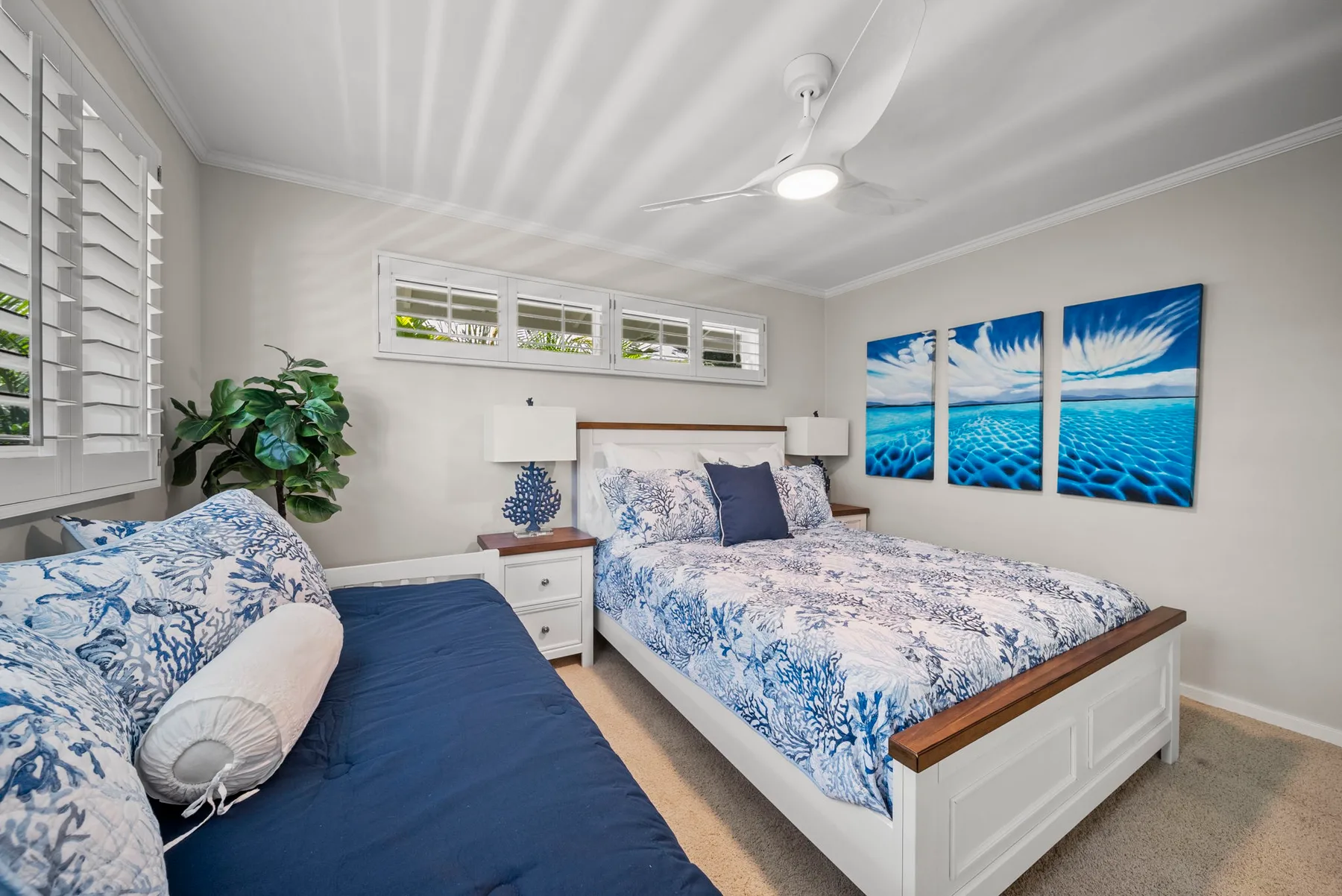 Dormitorio con dos camas, ropa de cama azul y blanca y arte de temática marina.