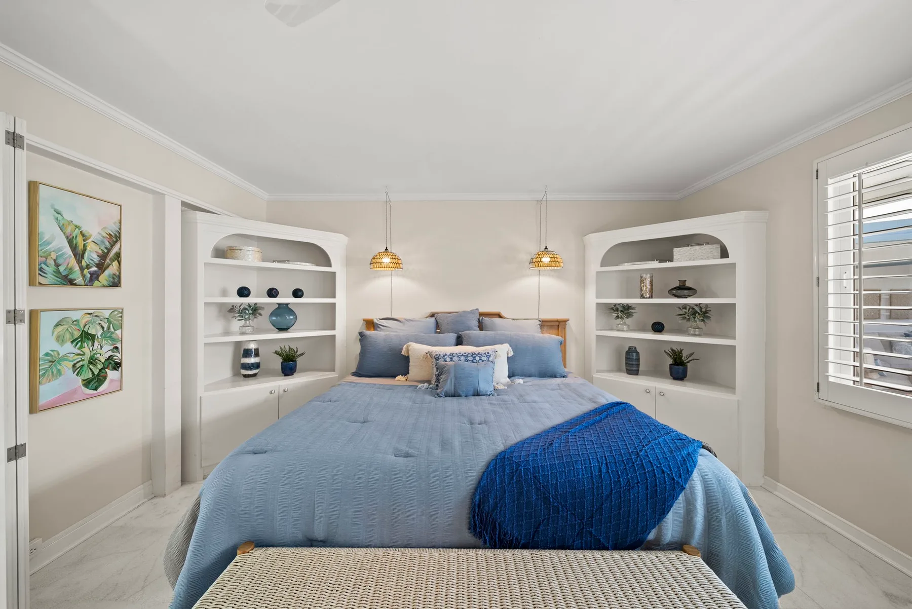 Un dormitorio con una cama vestida con ropa de cama azul entre estantes empotrados.