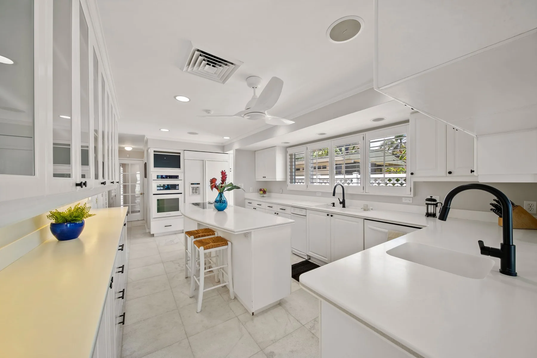 Una cocina blanca y luminosa con una isla central y ventanas grandes.