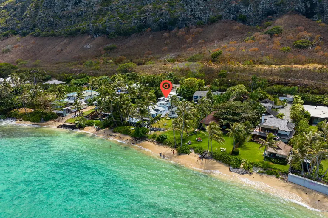 Vista aérea de una costa tropical con agua turquesa, playa de arena y casas entre palmeras.