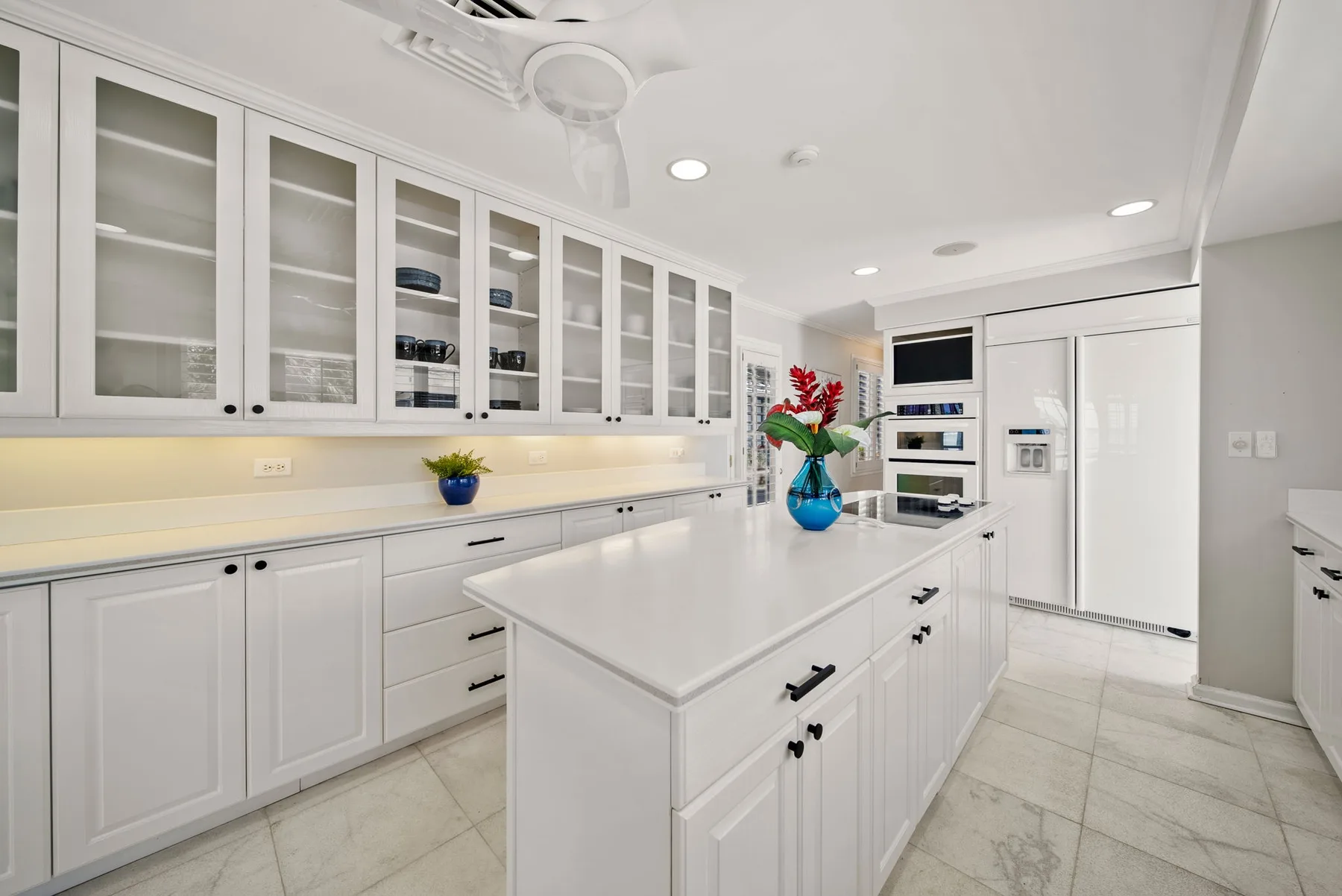 Una cocina blanca y luminosa con vitrinas de vidrio y una gran isla central.