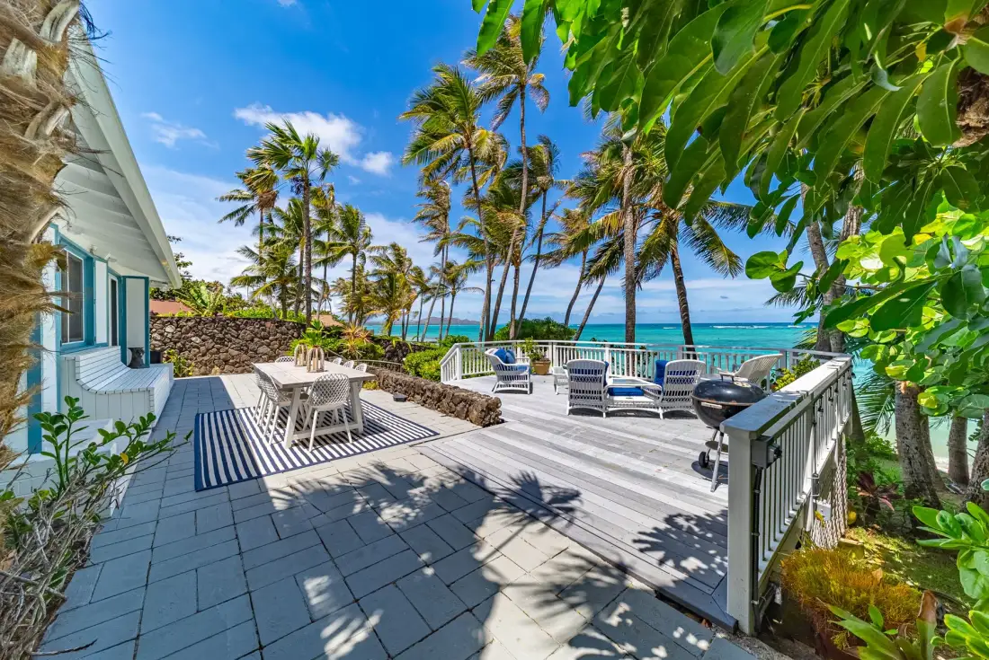 Una terraza junto al mar con asientos al aire libre, palmeras y vistas al océano.