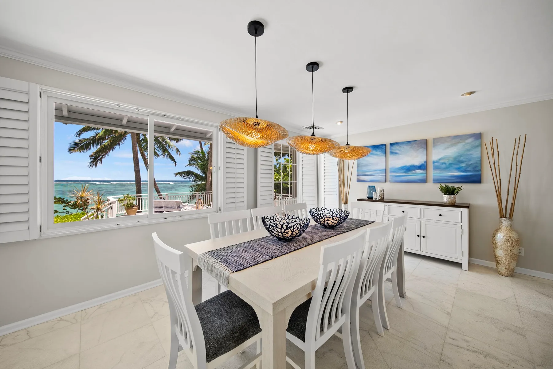 Un comedor luminoso con asientos blancos, lámparas colgantes y grandes ventanas con vista al mar.