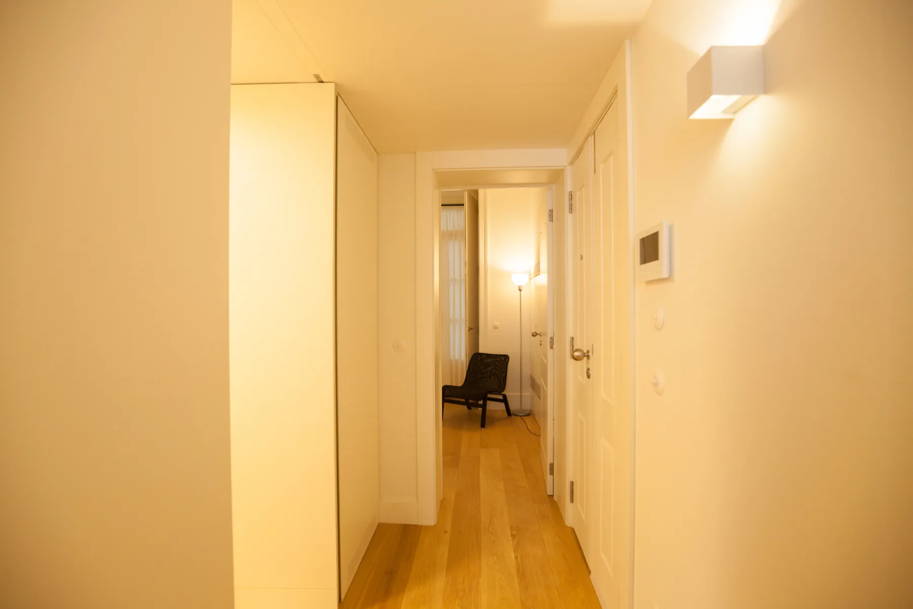 Un pasillo luminoso con suelo de madera y una silla al fondo.
