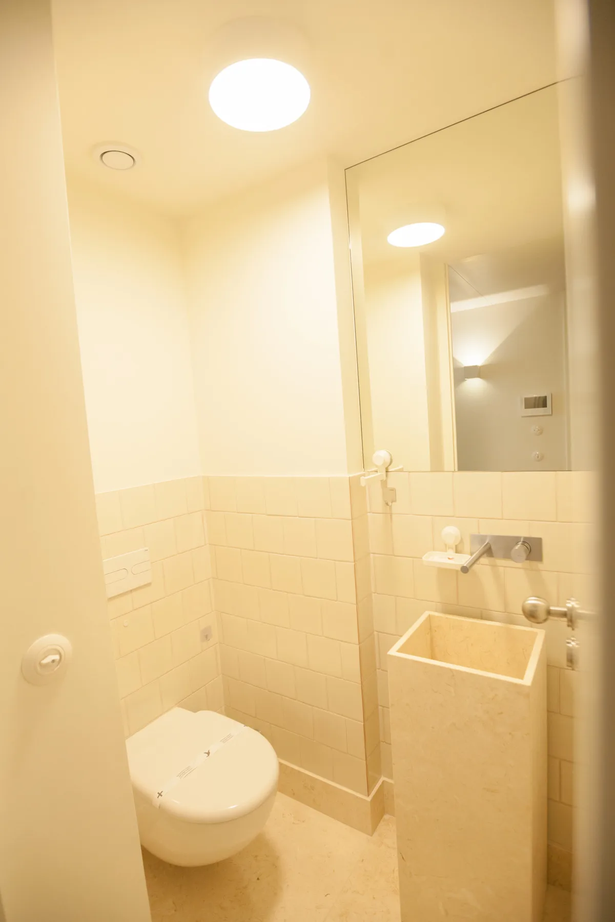 Un baño compacto con inodoro, lavabo de pared y espejo.