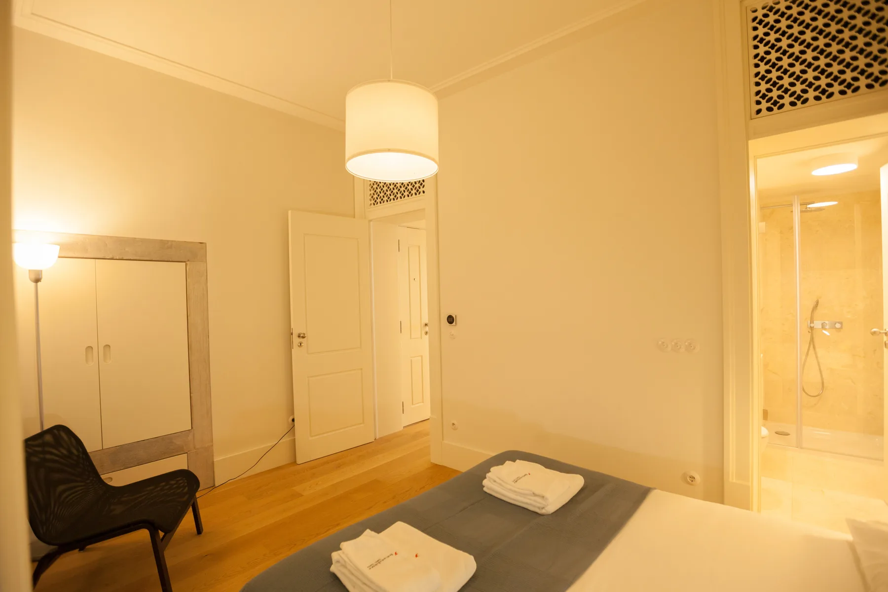 A bedroom with a bed, a dark accent chair, and a lit bathroom doorway.