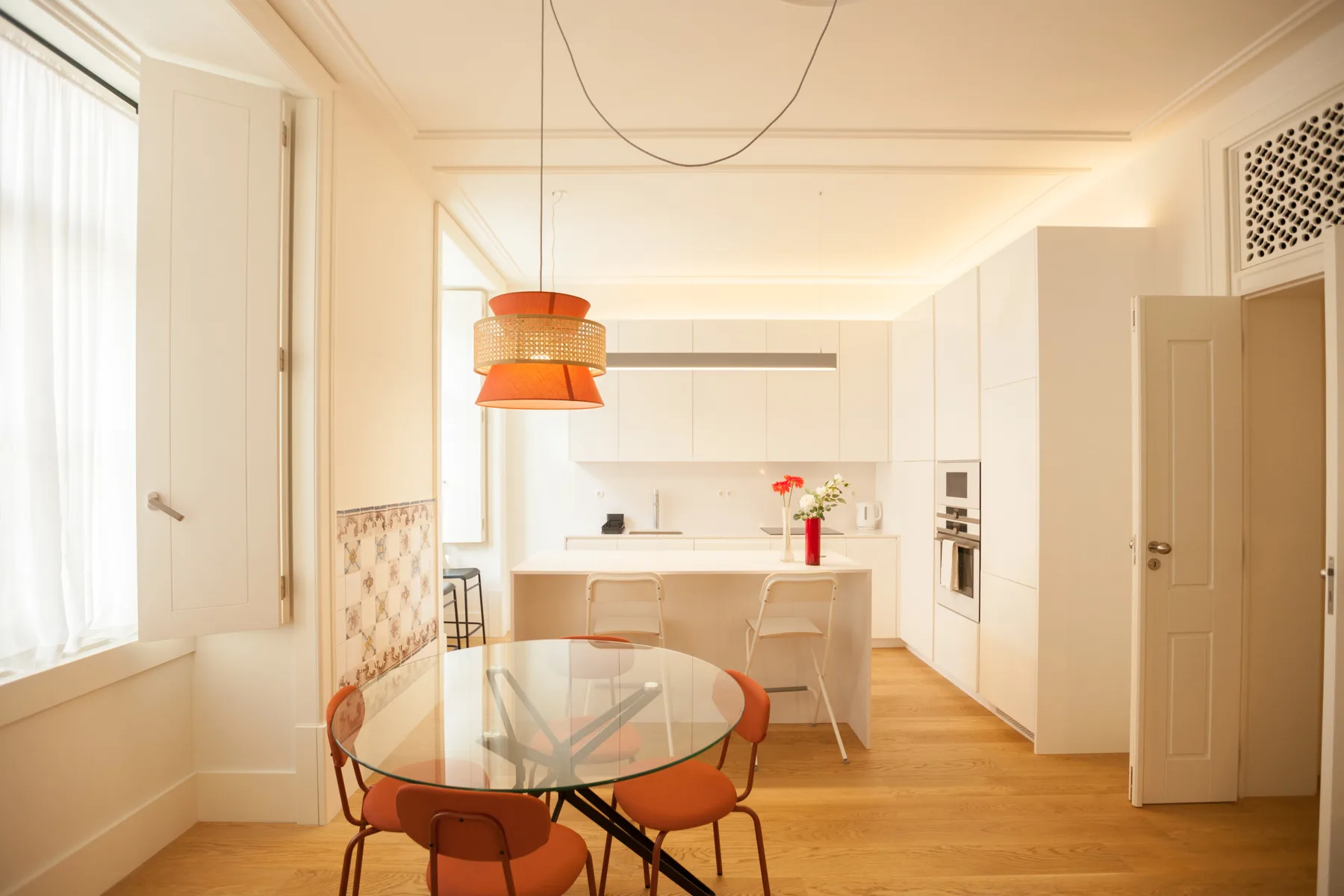 Cocina y comedor luminosos de planta abierta, con una mesa de vidrio y una lámpara colgante.