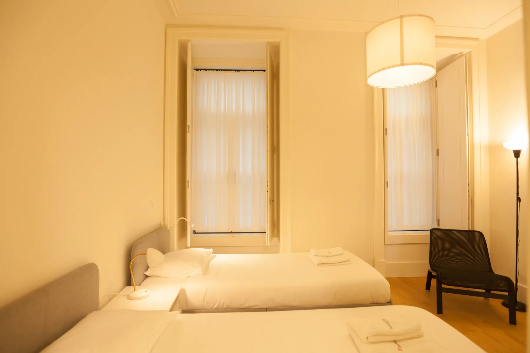 Un dormitorio con dos camas, ventanas altas e iluminación cálida.