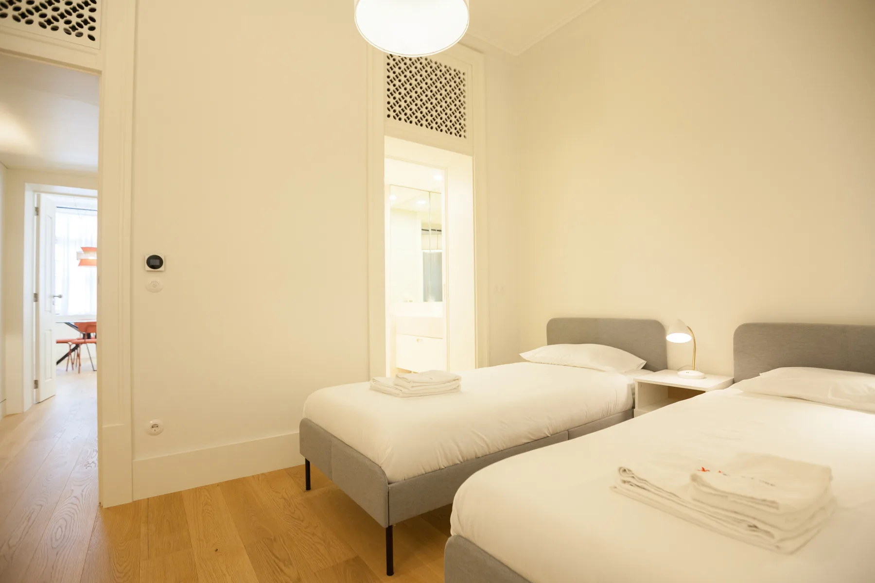 A bright bedroom with two beds, bedside tables, and light wood flooring.