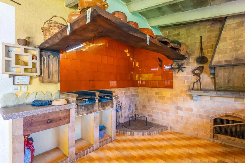 A rustic kitchen with a tiled cooking area and a large wooden hood.