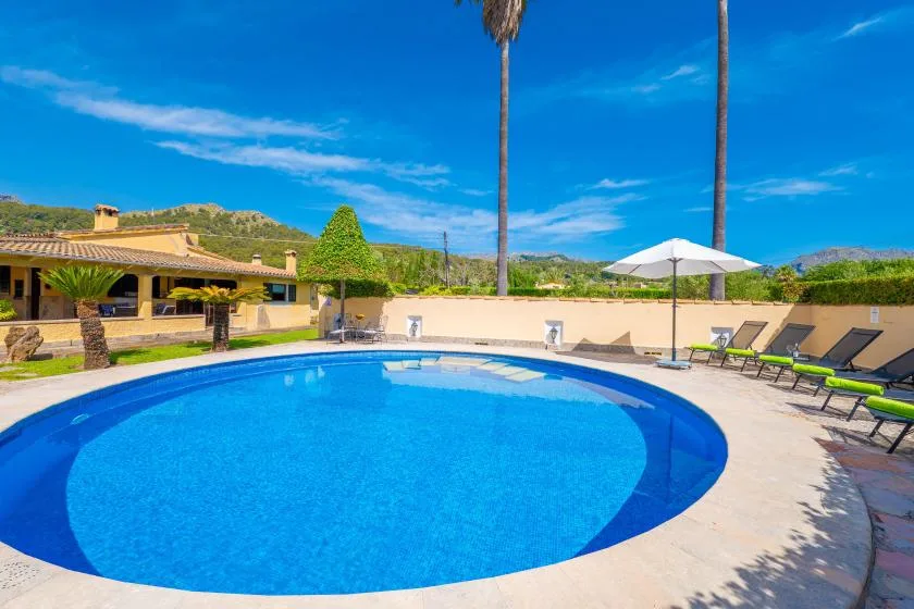 An outdoor swimming pool sits beside a patio with loungers and an umbrella.