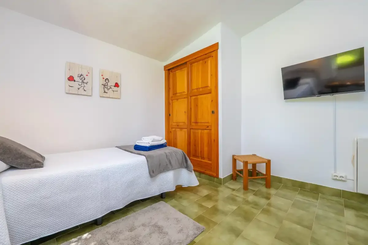 A bedroom with a single bed, a wooden door, and a wall-mounted television.