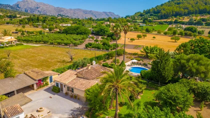 A rural property with a swimming pool amid fields and green hills.