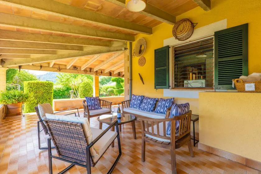 A covered outdoor seating area with patterned cushions and a view of the garden.