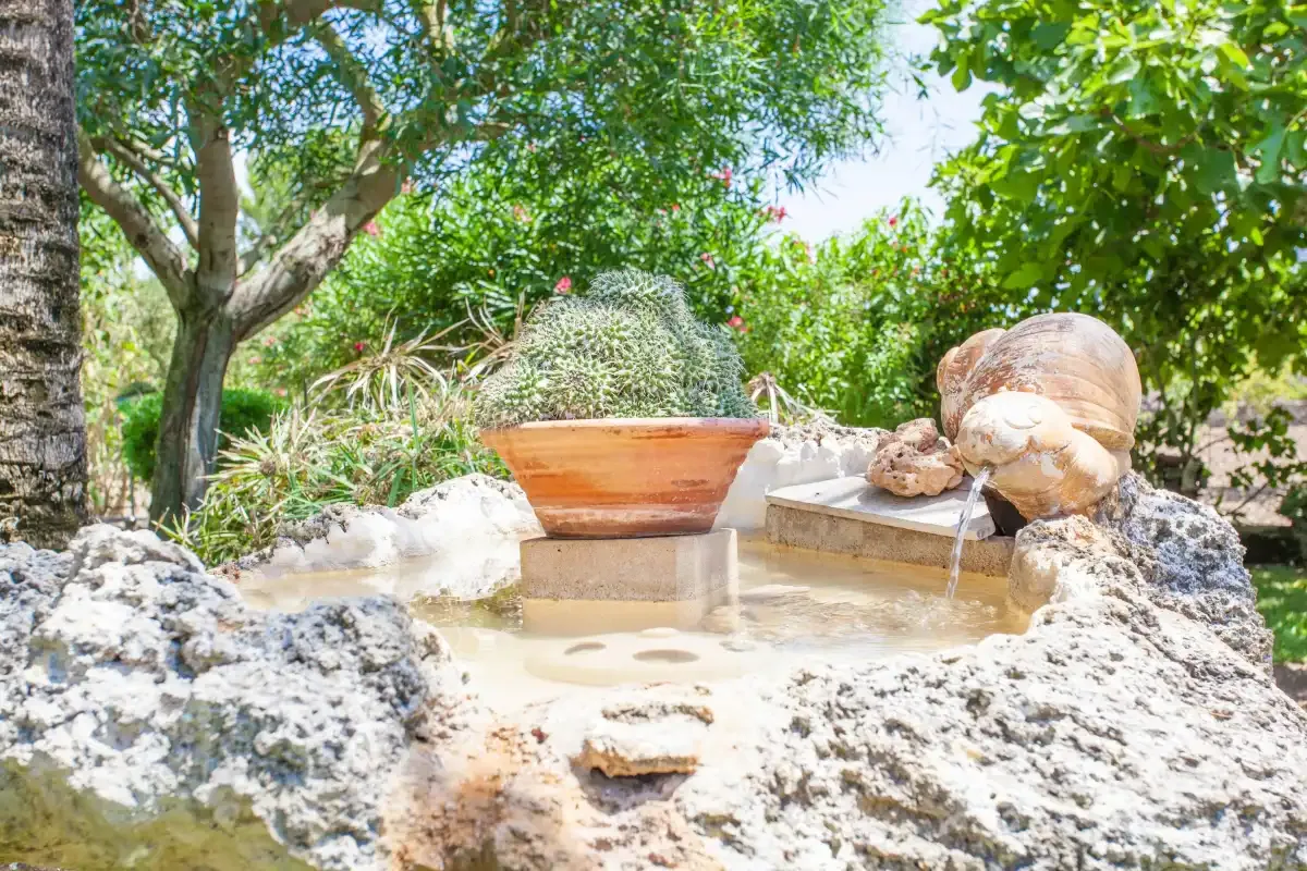 A garden fountain sits among rocks and leafy trees.