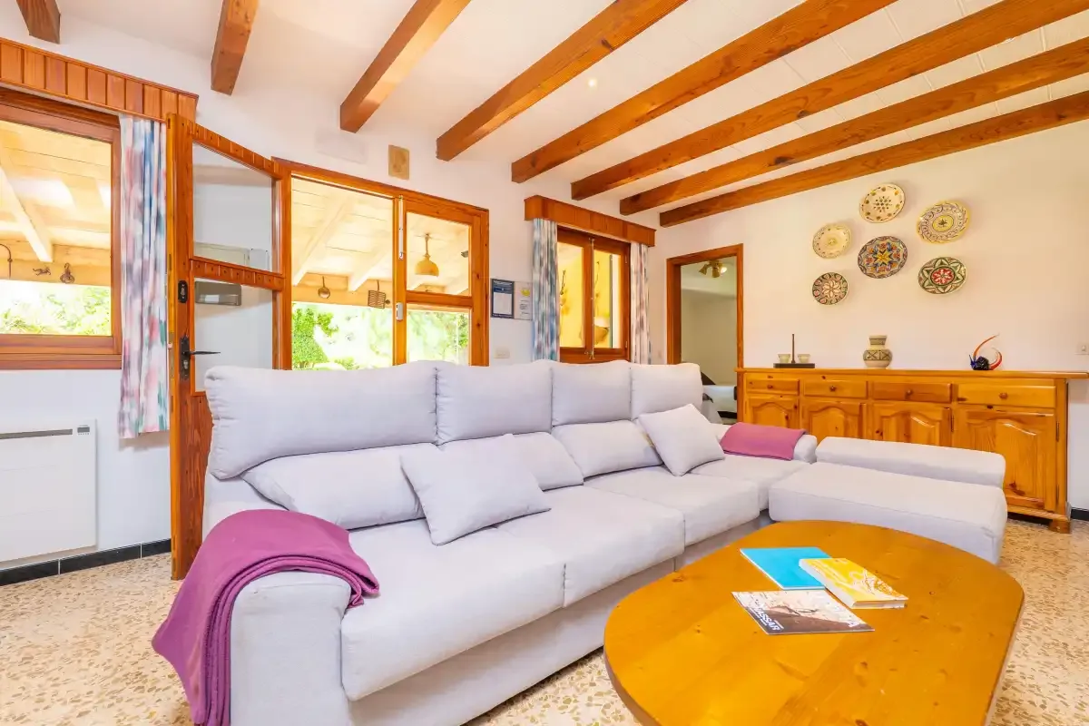 A bright living room with a large sectional sofa and wooden ceiling beams.