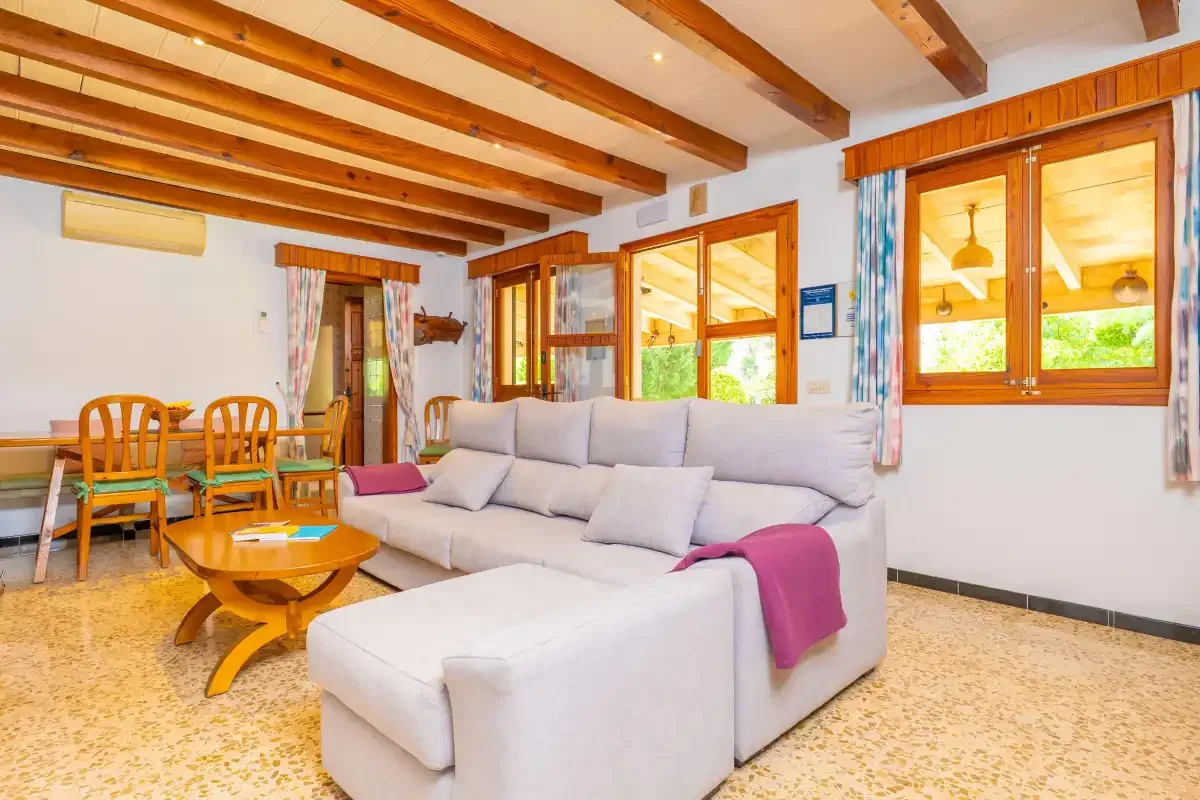 A bright living room with seating, wooden ceiling beams, and windows.