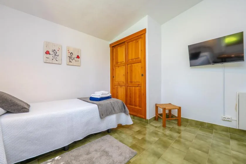 A bedroom with a single bed, wooden door, and wall-mounted television.