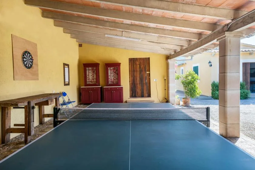A covered recreation area with a blue table tennis table and dartboard.