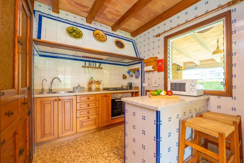 A tiled kitchen with wooden cabinets, a central counter, and a window.
