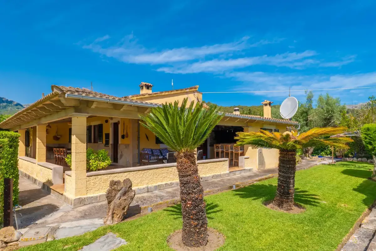 A single-story house with a covered veranda, palm trees, and a lawn.