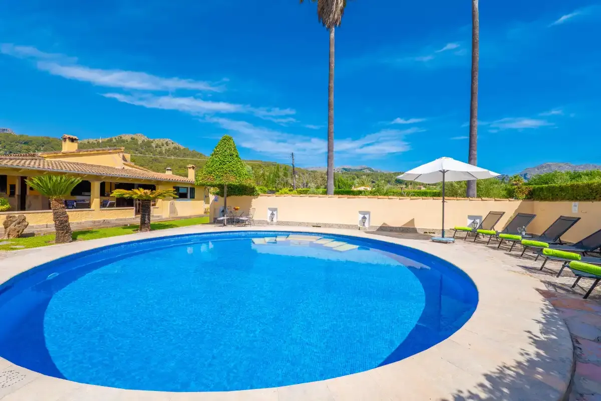 An outdoor swimming pool sits beside a paved patio with lounge seating.