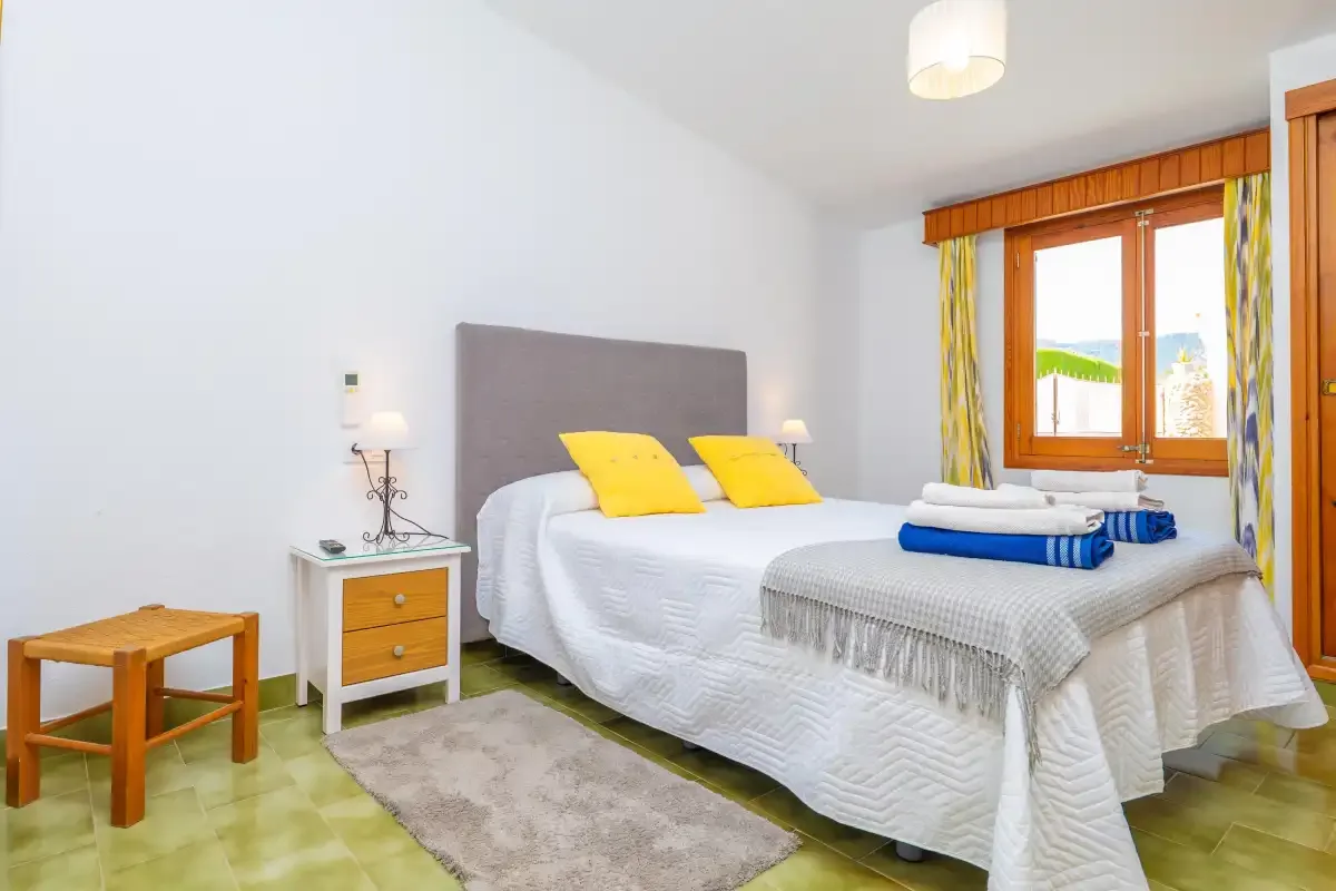 A bright bedroom with a large bed and a window dressed with colorful curtains.