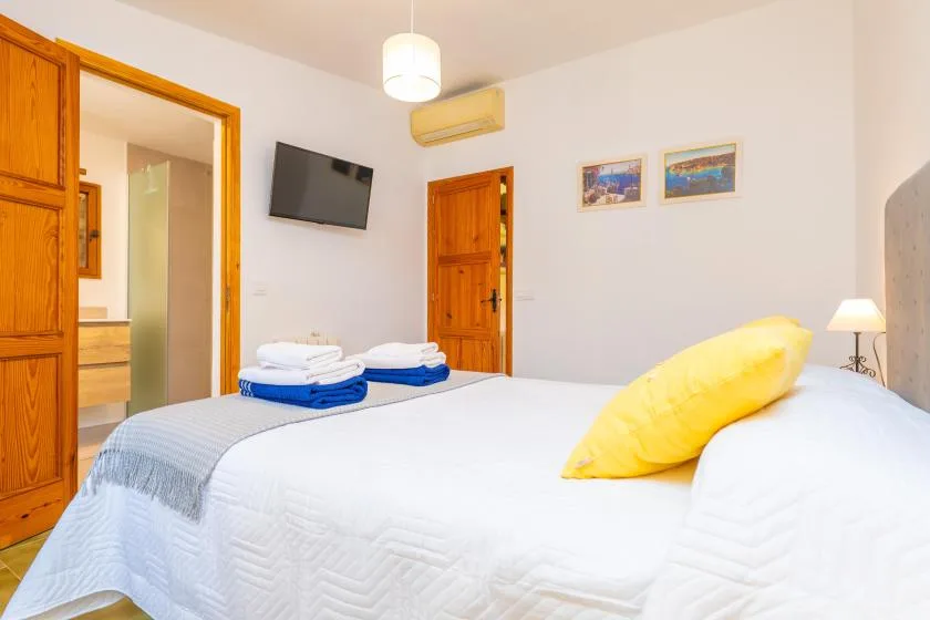 A bright bedroom with white bedding, a yellow pillow, and wooden doors.