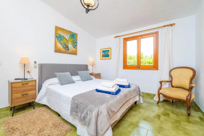 A bedroom with a made bed, bedside tables, and a window overlooking greenery.
