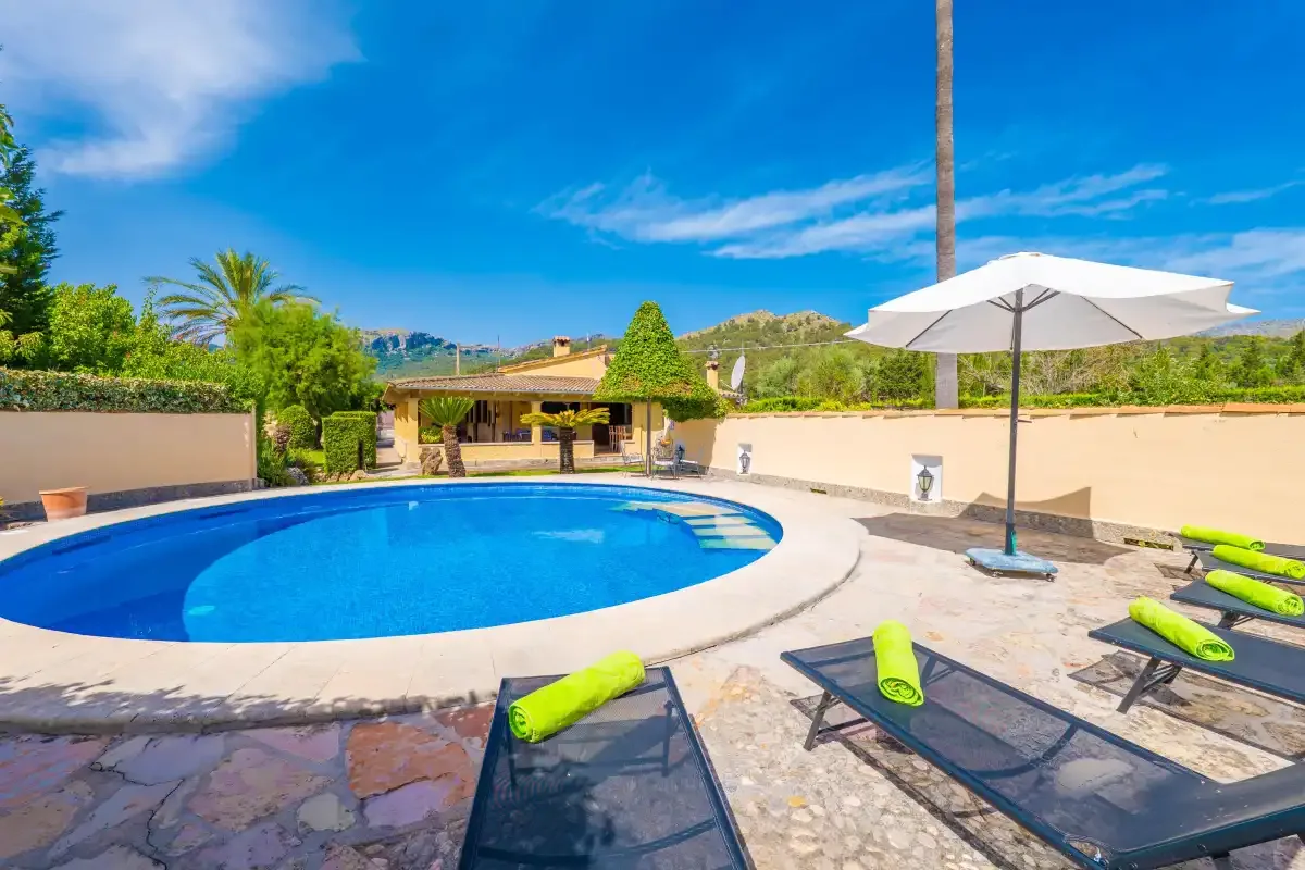 An outdoor swimming pool sits beside lounge seating and a white sun umbrella.