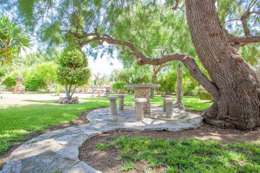A shaded garden seating area with a stone table and surrounding trees.