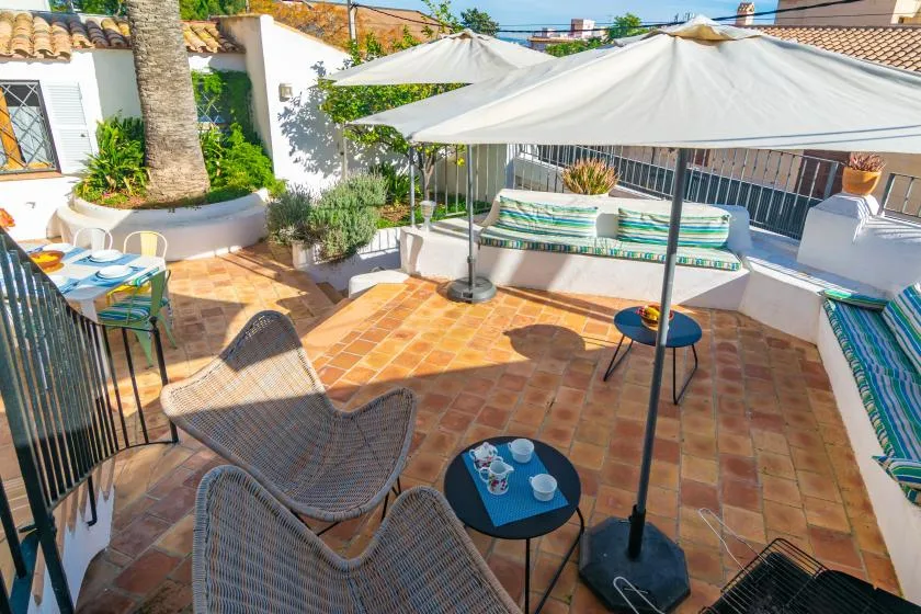 A sunny tiled terrace with seating, small tables, and a large shade canopy.