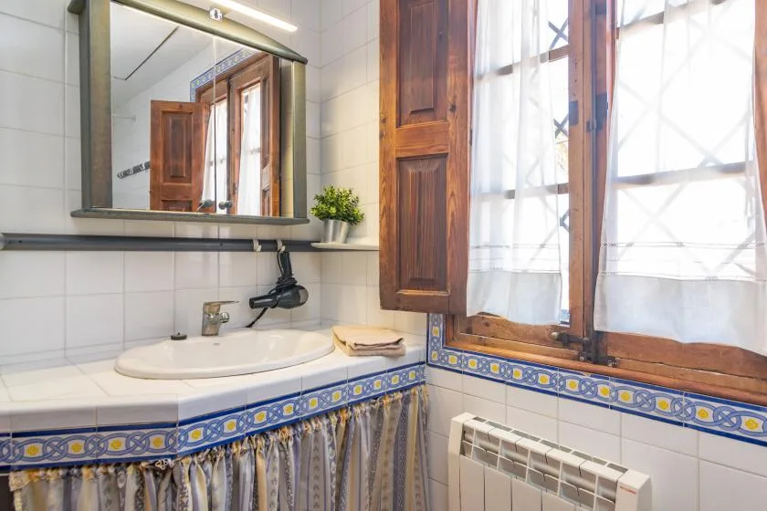 A tiled bathroom with a sink, mirror, and a curtained window.